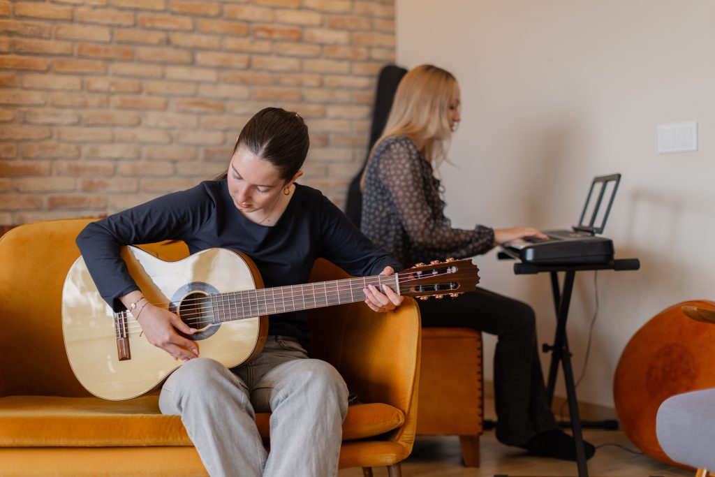 two young women playing guitar and keyboard in cozy living room